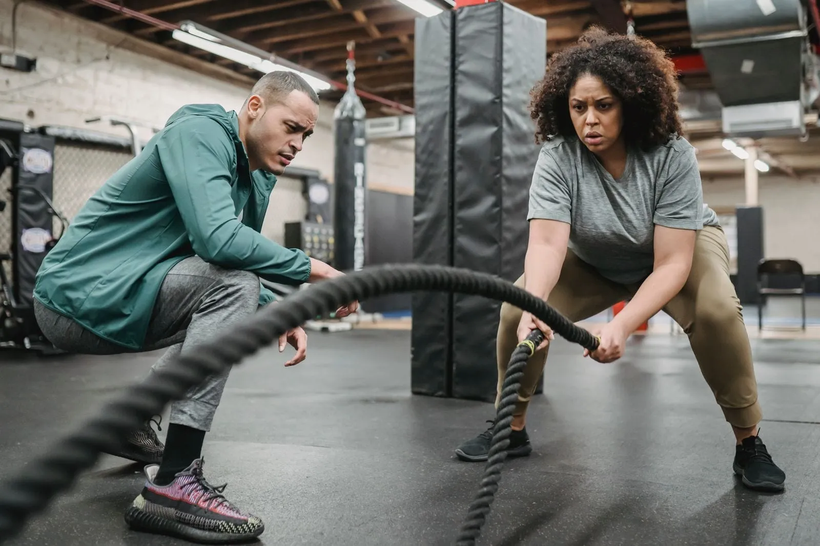 Anjana working battle ropes with her trainer crouched beside her