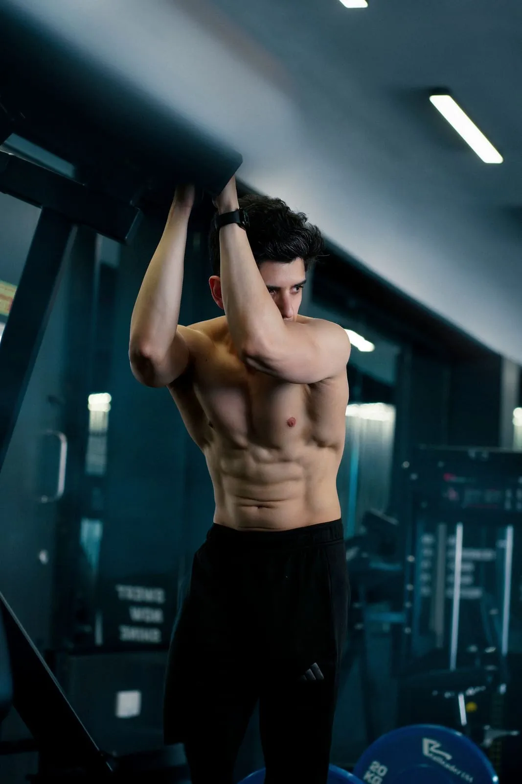 Bibek gripping an overhead bar, arms flexed
