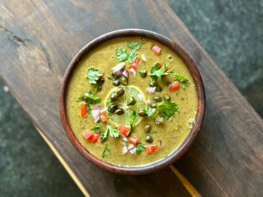 A bowl of dal topped with fresh coriander, green chilli and a slice of lime