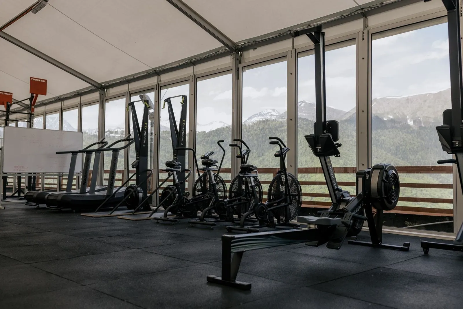 Bikes and rowers lined up along floor-to-ceiling windows with mountains outside