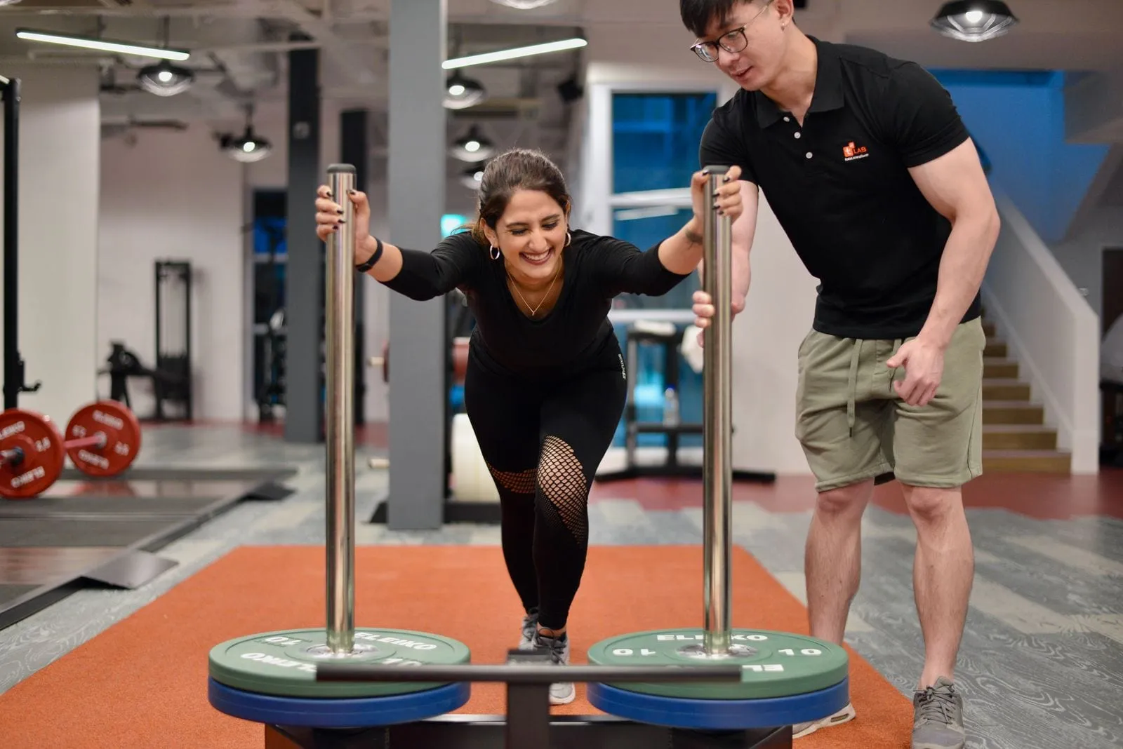 Trainer watching a member push a weighted sled on the gym floor