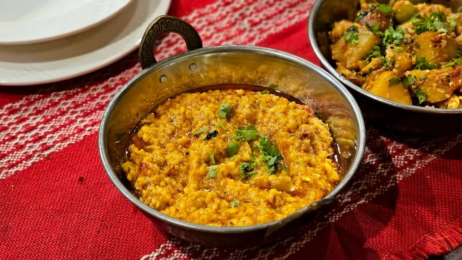 A bowl of dal tadka topped with herbs on a patterned cloth