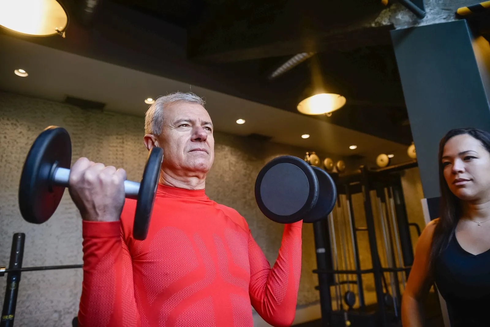 David pressing a pair of dumbbells overhead in the gym