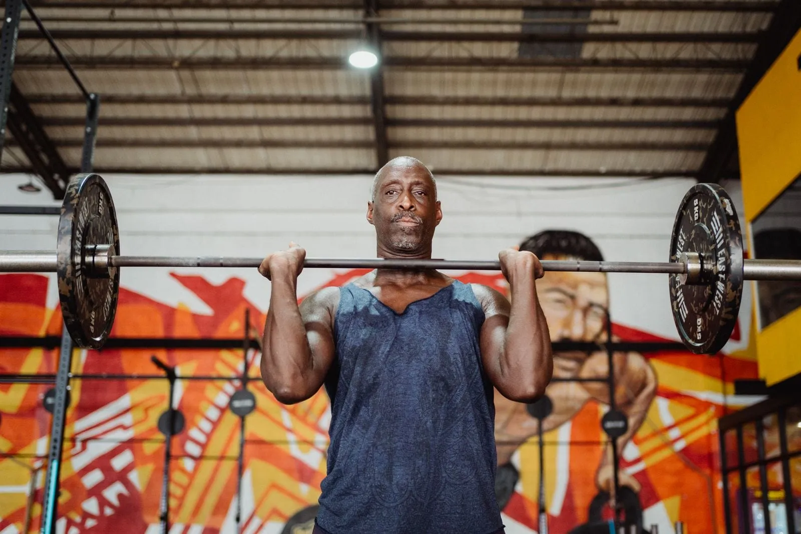 Krishna holding a barbell at his shoulders in the gym