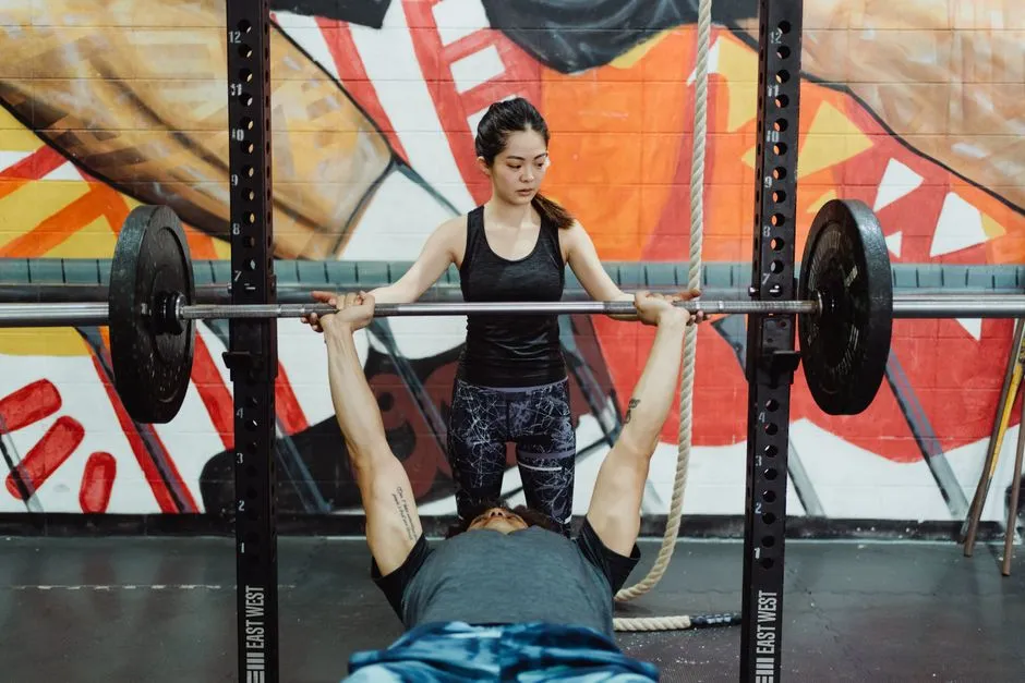 A man pressing a barbell on a flat bench in a rack while a woman stands behind him to spot