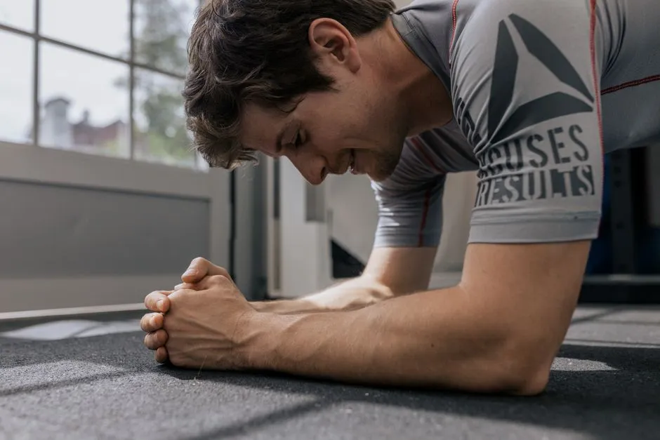 A man holding a forearm plank on the floor of a gym