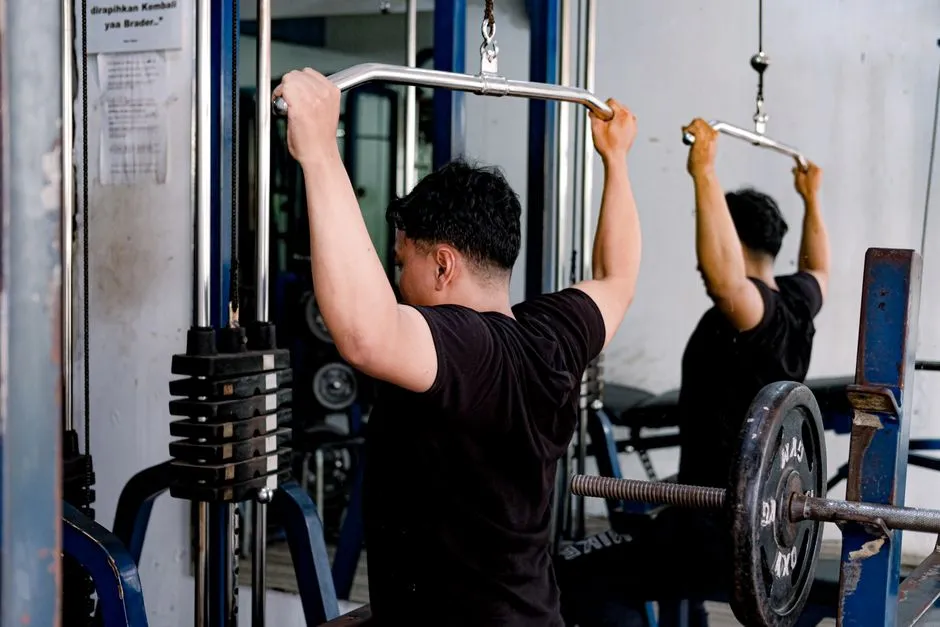 A man pulling the bar of a lat pulldown machine in a gym, seen from behind