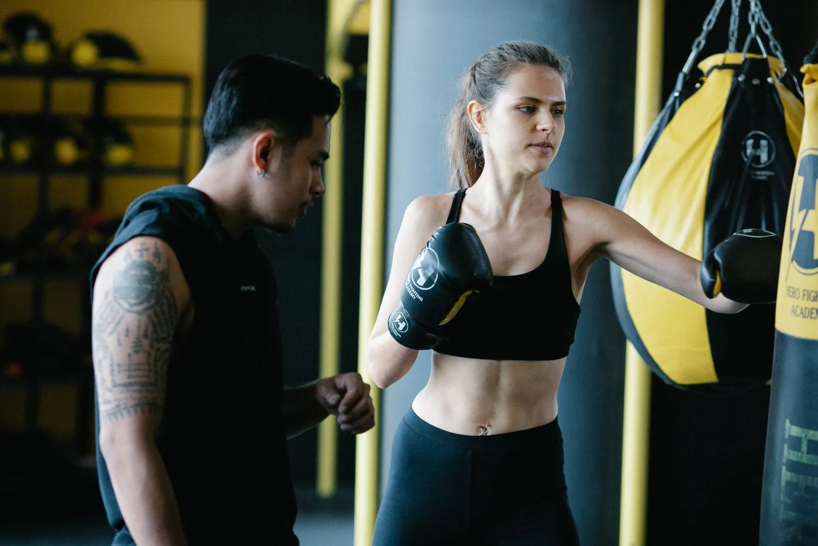 Priya in boxing gloves, guard up, while her coach watches