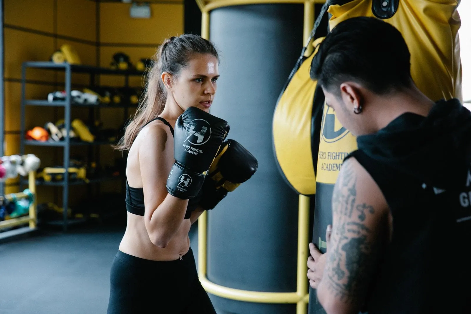 Priya throwing a punch at a heavy bag with her coach beside her