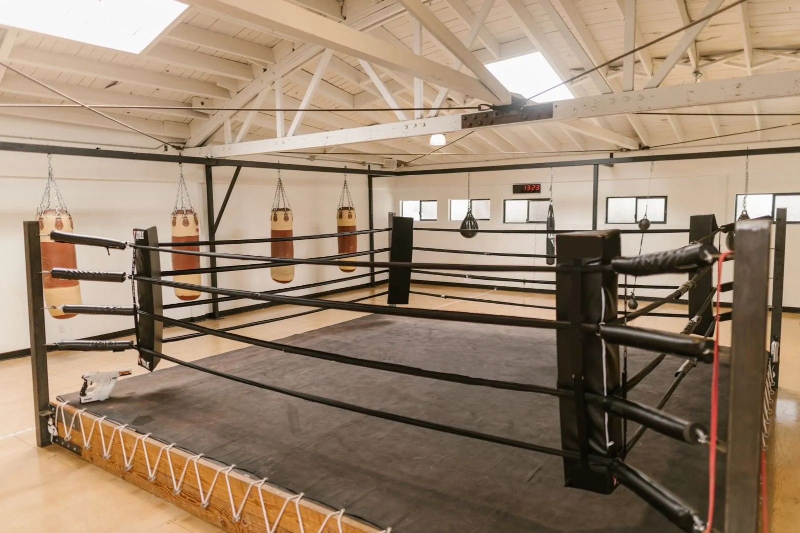 Full-size boxing ring on a wooden floor with bags along the walls