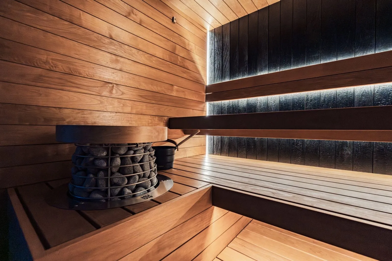 Dark wood sauna with a stone heater and soft lights under the benches