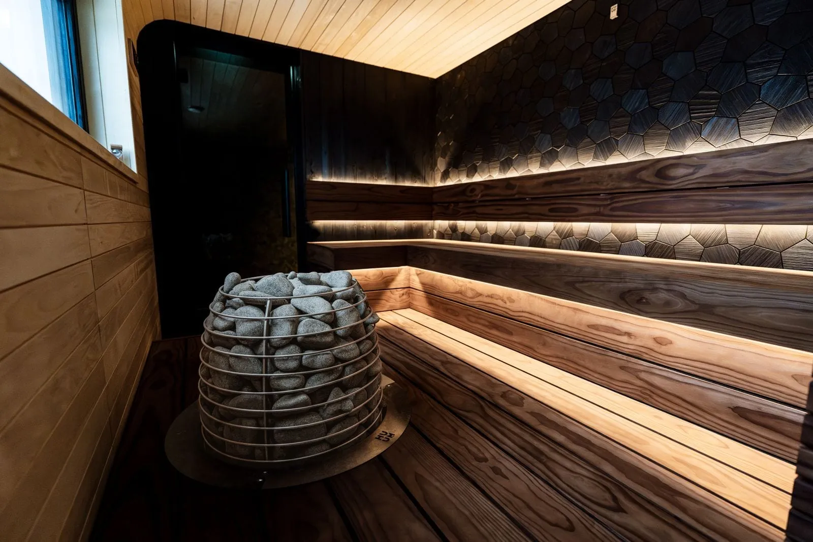 Dark wood sauna with warm lights under the benches and a stone heater