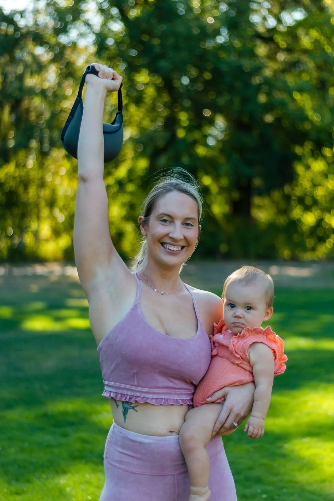 Tara smiling outdoors, holding her baby daughter after a workout