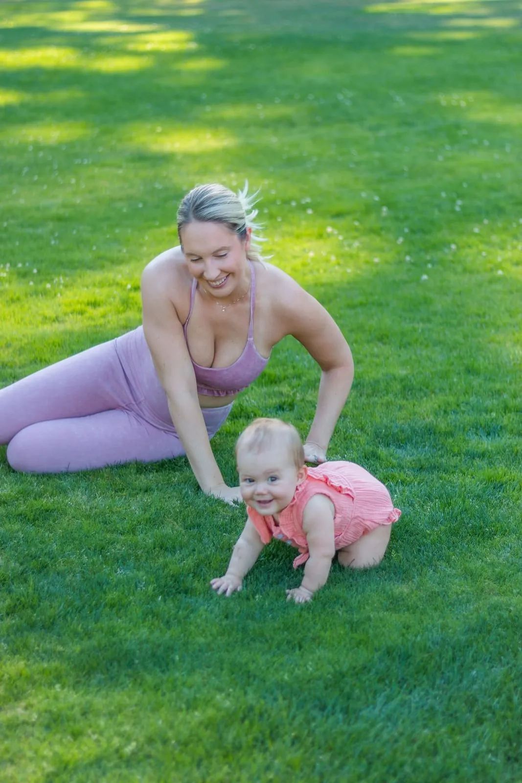 Tara doing floor exercises on the grass next to her baby