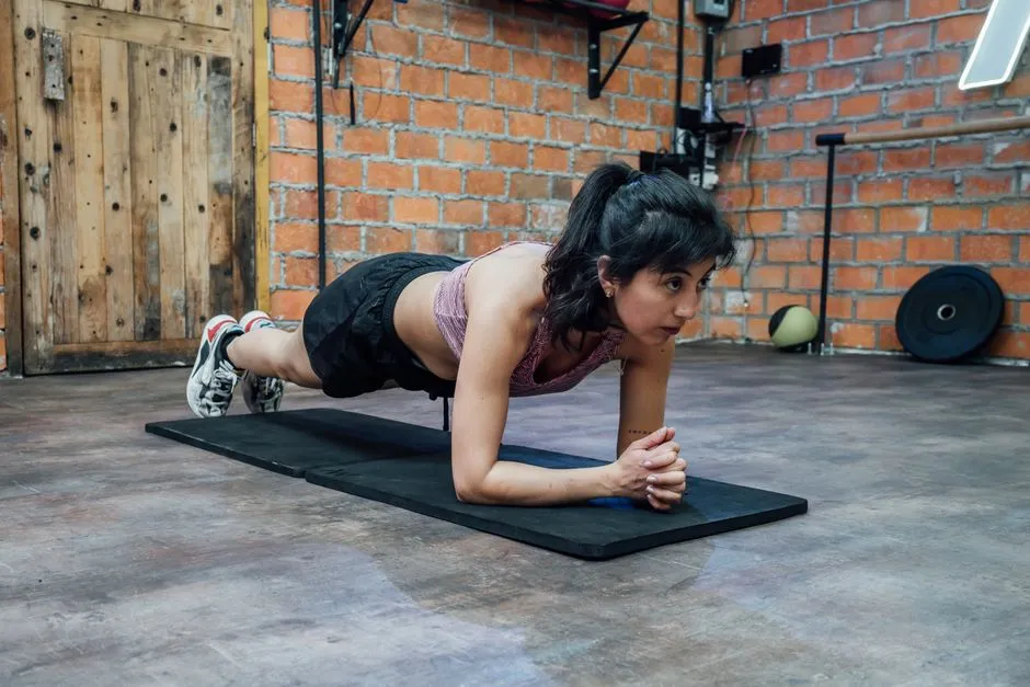 A woman holding a forearm plank on a mat on a gym floor